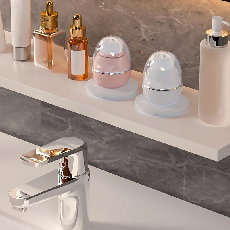 Facial Cleansing Brush - Two egg-shaped cleansing brushes on a bathroom shelf with skincare bottles and a chrome faucet