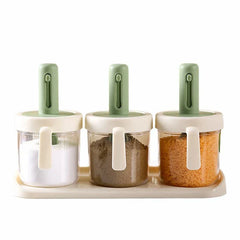 Spice Jar - Three matching clear storage canisters with white and sage green lids holding salt, pepper, and red spice arranged on a cream plastic base tray
