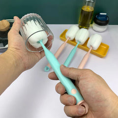 Sponge Bottle Cleaning Brush - Two hands holding a clear glass and a mint handled sponge brush cleaning inside the glass, with three other brushes resting on a yellow tray in the background