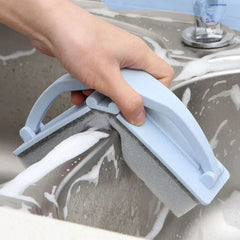 Cepillo de limpieza para ducha con esponja y estropajo sostenido en la mano cerca de una pared de la ducha