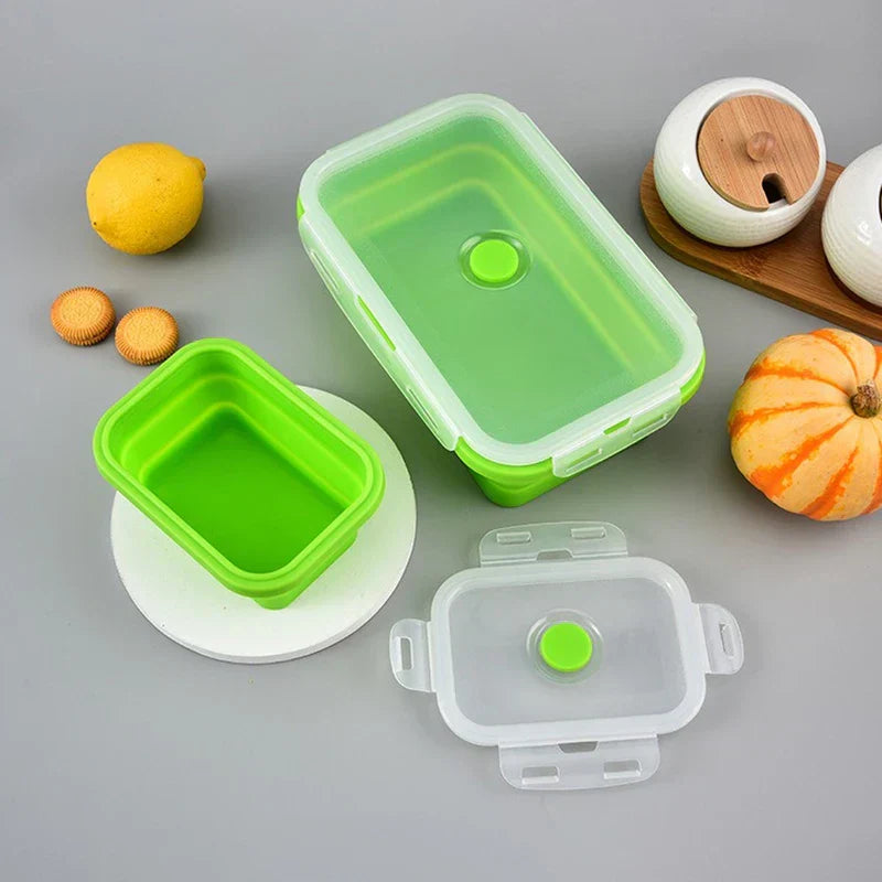 Food Storage Containers - Green and clear collapsible food containers, some open with lids off, arranged on a gray surface with small props around them