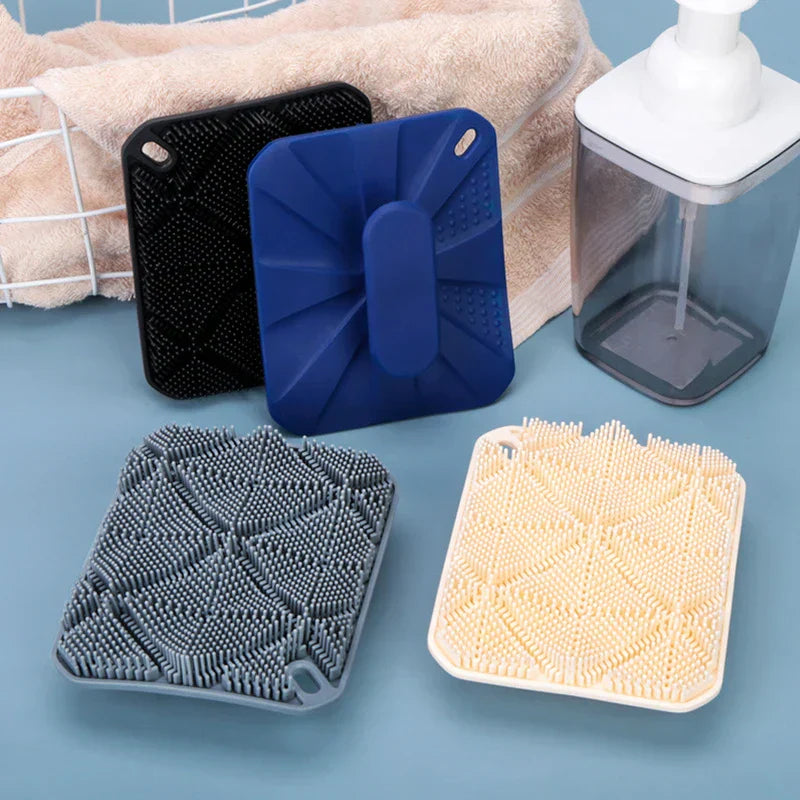 cepillo de ducha para el cuerpo - Cepillos limpiadores cuadrados de colores variados colocados sobre una encimera de baño junto a una toalla y un dispensador de jabón