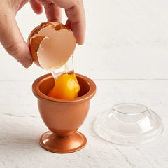 Stainless Steel Egg Ring Mold - Hand pouring a cracked raw egg into a copper egg cup, clear lid resting beside it on a white surface.