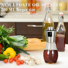 Oil Sprayer Mister - Glass and stainless steel oil sprayer filled with dark liquid, placed on a kitchen counter beside fresh vegetables and two glass bottles
