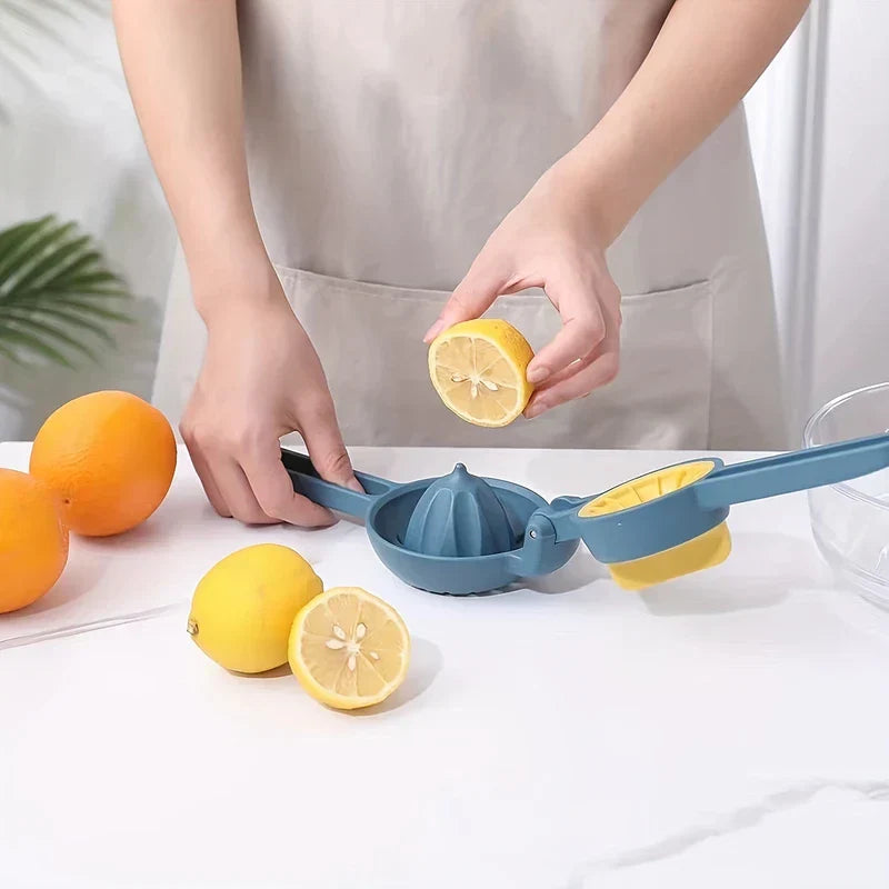 zitruspresse - Hände halten eine halbe Zitrone über eine geöffnete blaue Hand-Zitruspresse, mit ganzen Orangen und Zitronen auf weißer Arbeitsplatte