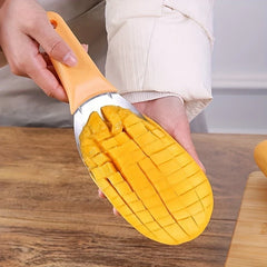 Hand holding mango slicer scooping cubed mango flesh from a half mango held over a wooden table