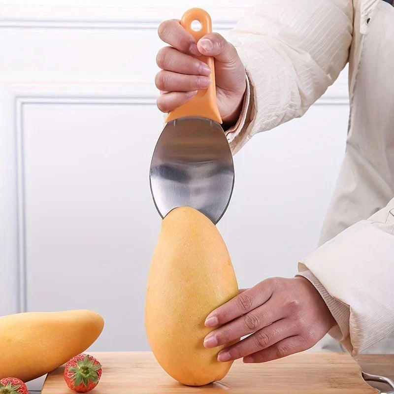 Hand holding a mango slicer above a whole mango on a wooden cutting board, with strawberries nearby