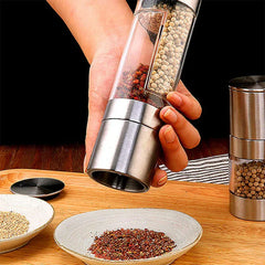 Spice Grinder Mill - Hand holding a dual-compartment spice grinder, grinding red spice into a ceramic dish on a wooden counter, second grinder sits to the right.
