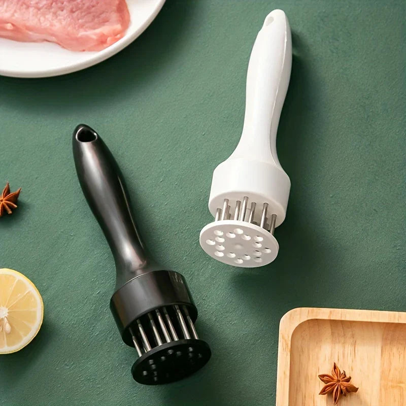 Stainless Steel Meat Tenderizer - Two meat tenderizers, one black and one white, placed on a green surface with lemon slice, star anise, raw meat and a wooden tray