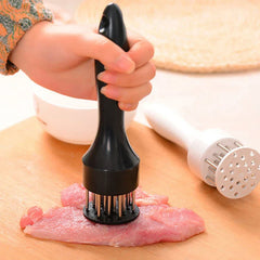Stainless Steel Meat Tenderizer - Hand pressing black handled tool into raw meat on a wooden cutting board, second white handled tool resting nearby