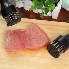 Stainless Steel Meat Tenderizer - Two black handled tools resting on a wooden cutting board next to a piece of punctured raw meat