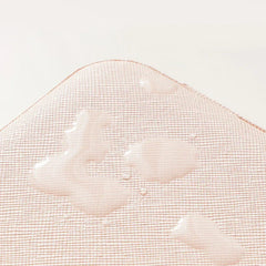 Organizador de almacenamiento tipo cubo de viaje: primer plano de superficie de tela texturizada rosa claro y curva con múltiples gotas de agua húmedas de distintos tamaños, sobre un fondo blanco hueso liso
