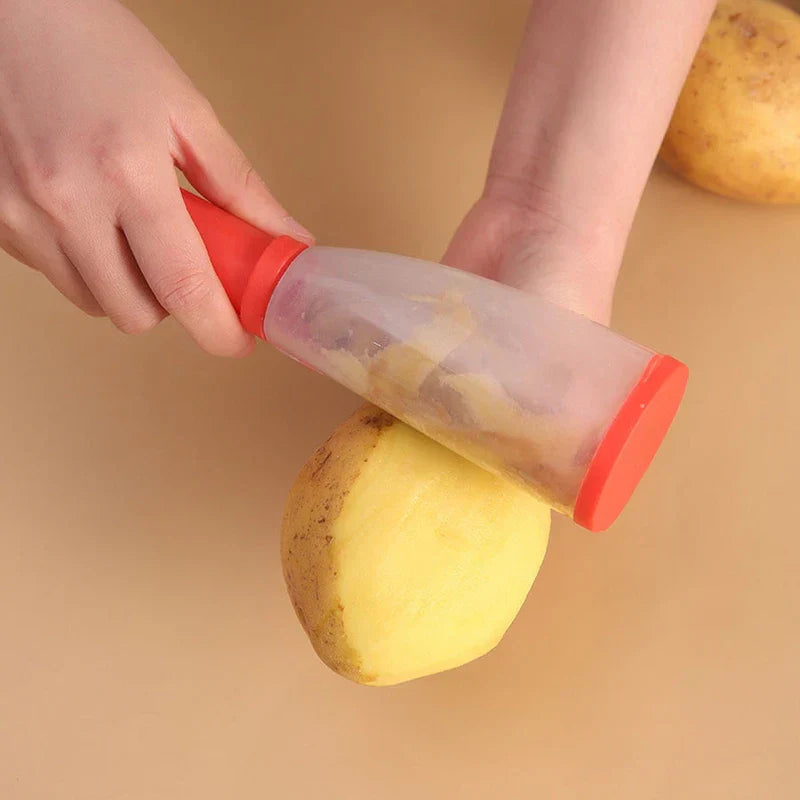 Storage Grater Box Container - Person using a red-handled peeler to peel a potato, with collected potato skins visible inside the clear catch chamber