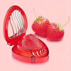 Red plastic strawberry slicer with an open lid holds a strawberry, two whole strawberries beside it on pink background