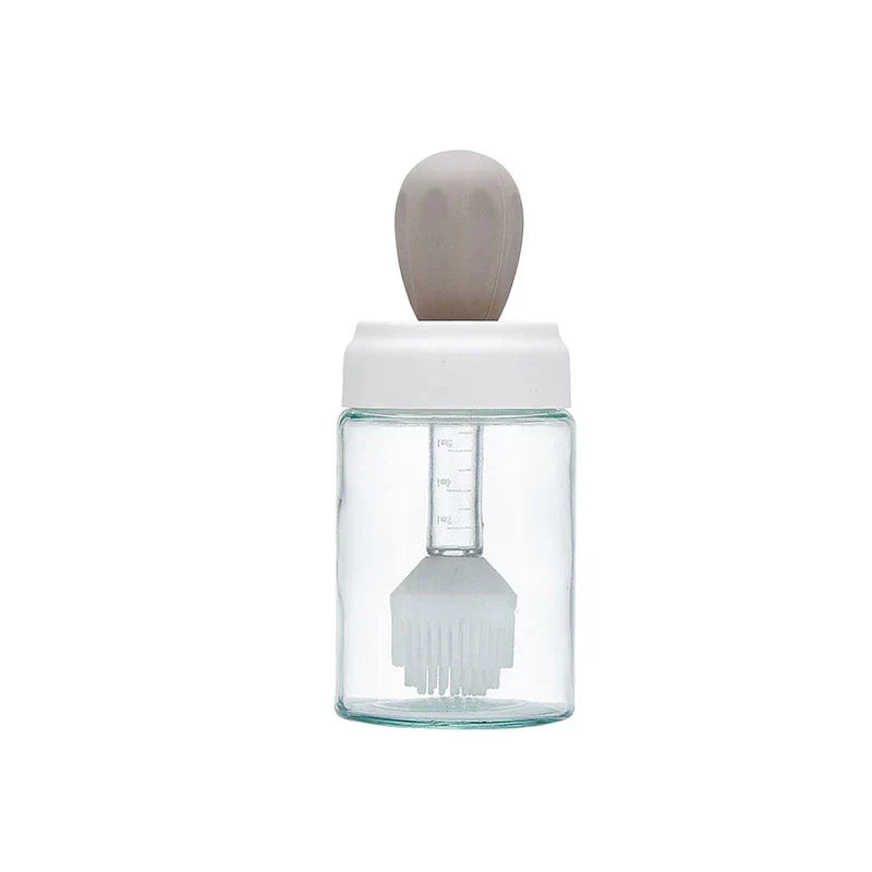 Glass Cleaning Squeegee - Clear glass jar with white lid, taupe silicone top handle, internal graduated dip tube and silicone basting brush, empty, studio shot on white background