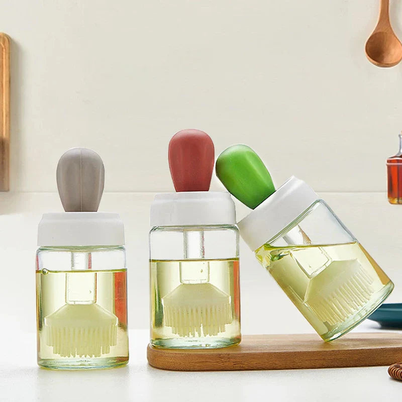 Glass Cleaning Squeegee - Three glass jars with white lids and gray, red, green silicone handles, two upright holding cooking oil, one tilted to show oil flow, arranged on a wooden kitchen board