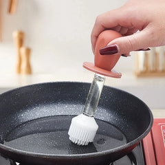 escurridor de vidrios - Mano con esmalte de uñas rojo oscuro sosteniendo un pincel para untar con mango rojo, extendiendo aceite sobre la superficie de una sartén antiadherente negra con motas