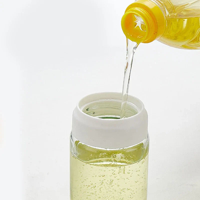 Glass Cleaning Squeegee - Yellow oil bottle pouring cooking oil into an open glass oil bottle with a white plastic collar.