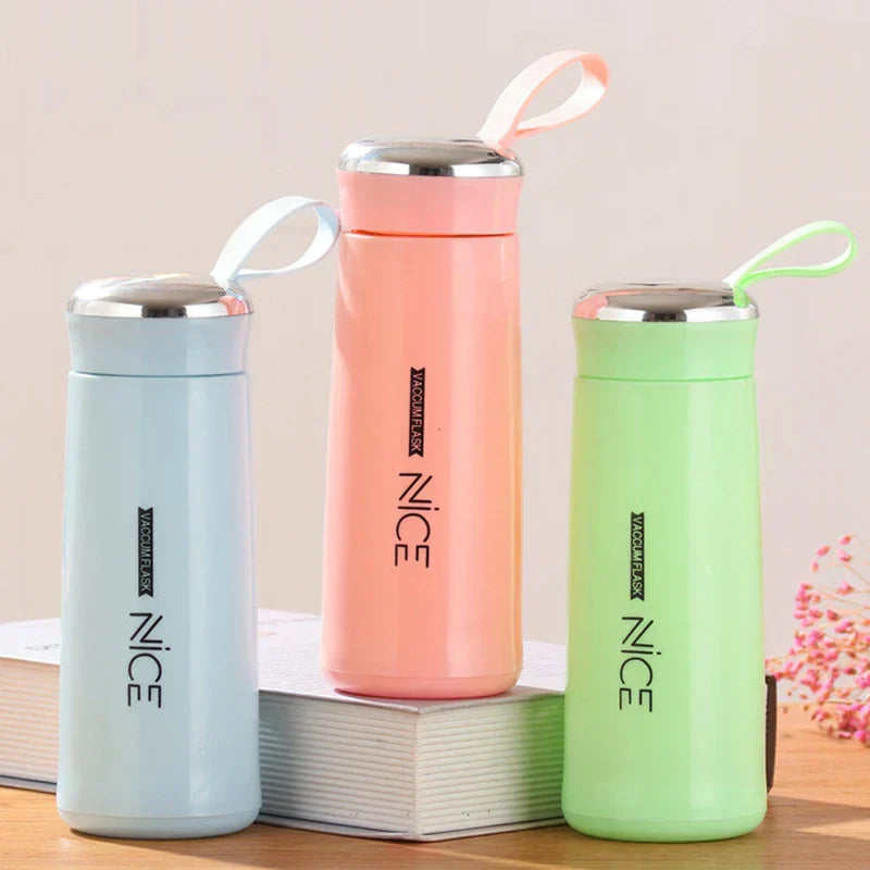 Light blue, peach, and green plastic tumbler cups with wrist straps arranged on books, on a wooden surface