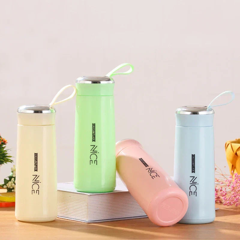 Four plastic tumbler cups in cream, light green, pink, and light blue arranged on and around a book on a wooden table.