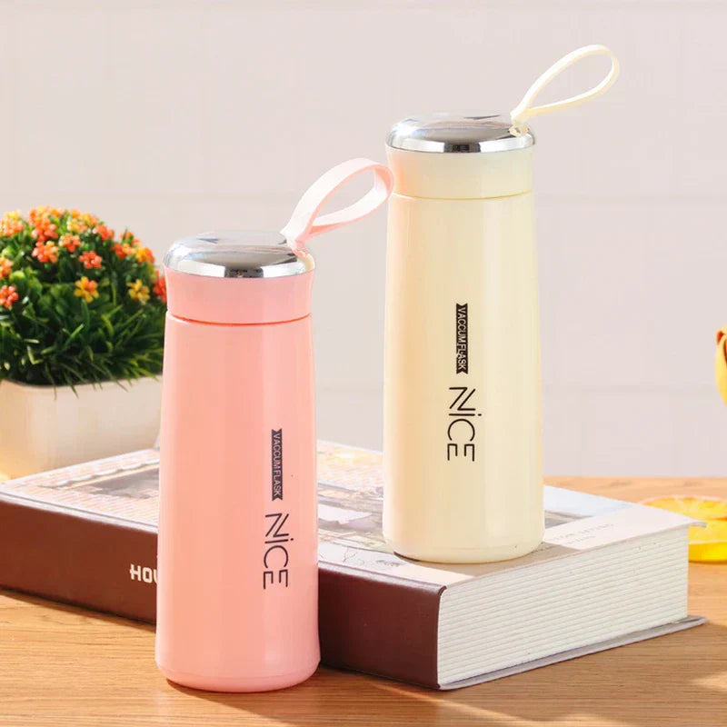 Pink and cream plastic tumbler cups rest on a book, with a small potted plant in the background.