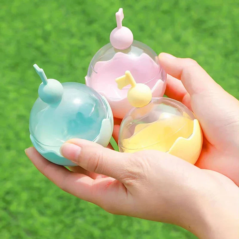 Ice Ball Mold - A hand holds three small spherical pastel-colored plastic containers against a green grass background.