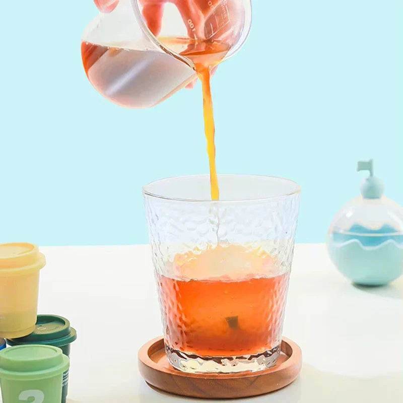 Ice Ball Mold - Brown liquid pours from a small glass pitcher into a textured glass; the blue spherical container sits on a white table.