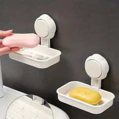 Soap Dish Holder - Two white wall-mounted soap dish holders attached to a dark wall; a hand holds a pink bar of soap near the upper holder, and a yellow soap bar rests in the lower holder