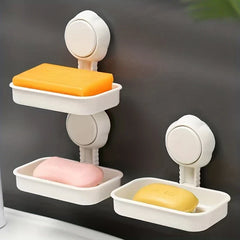 Soap Dish Holder - Three white wall-mounted soap dish holders on a dark wall; two are stacked vertically holding orange and pink soap bars, one sits to the right with a yellow soap bar
