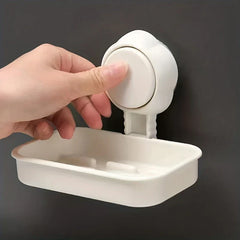 Hand presses the suction dial of a white wall-mounted soap dish holder against a dark wall