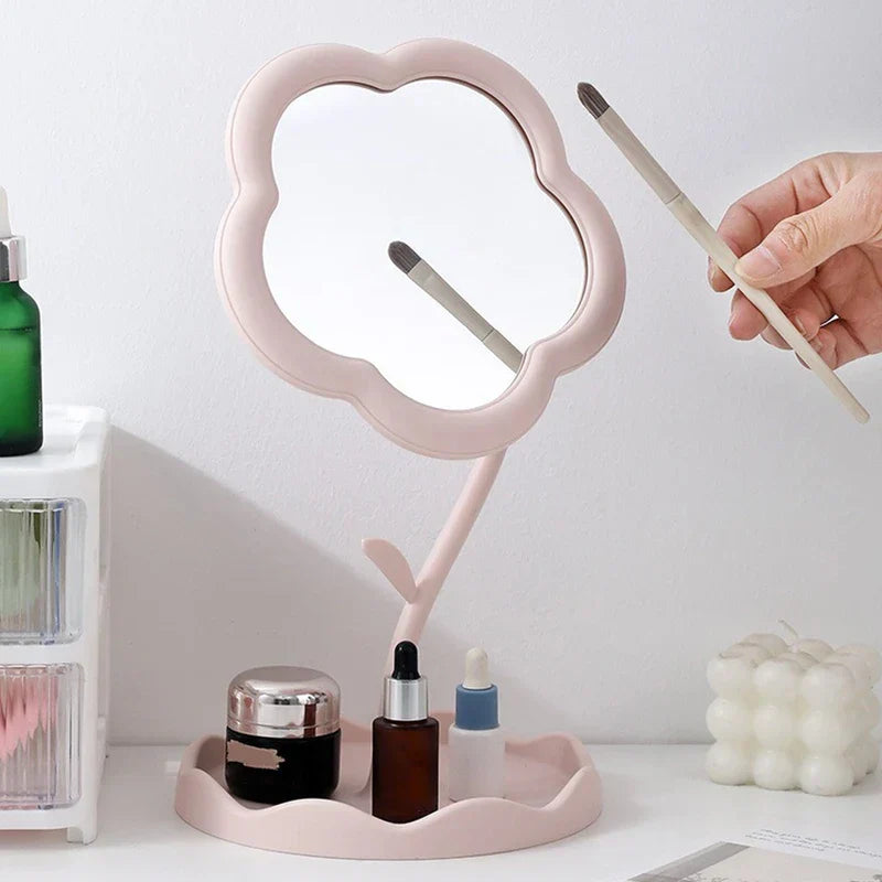 Makeup Mirror - Light pink flower-shaped desktop mirror reflecting a makeup brush held by a hand, with skincare items on its tray
