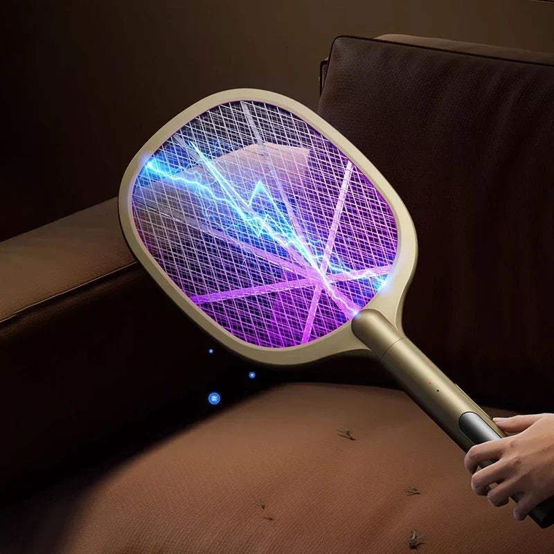 matamoscas eléctrico - Mano sosteniendo un matamoscas eléctrico dorado claro sobre un sofá marrón, arcos eléctricos azules visibles a través de la rejilla iluminada en púrpura, insectos muertos en la superficie del sofá