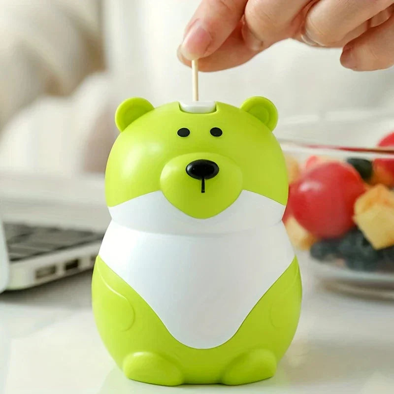 Sujetapalillos con forma de osito de peluche: una mano sacando un palillo de madera de la parte superior de un recipiente verde lima con forma de oso de dibujos animados