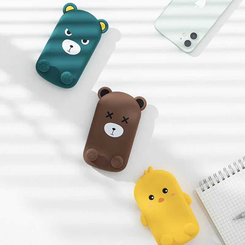 Folding Phone Stand - Three cartoon shaped items (two bears, one yellow chick) laid flat on a white striped surface near a smartphone and notepad