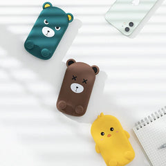 Folding Phone Stand - Three cartoon shaped items (two bears, one yellow chick) laid flat on a white striped surface near a smartphone and notepad