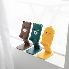 Folding Phone Stand - Three cartoon character themed folding stands (two bears, one yellow chick) placed upright on a white window ledge
