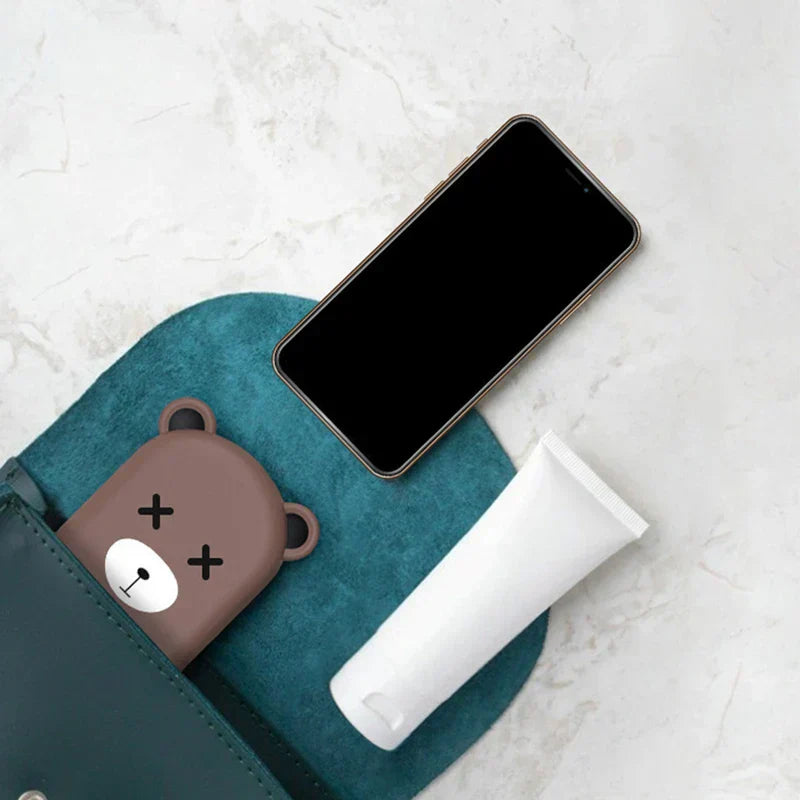 Folding Phone Stand - Flat lay of brown bear case/charger partially in teal bag, black smartphone, white tube on marble background