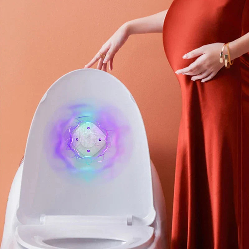 Sanitizer Light – Schwangere Frau berührt den offenen weißen Smart-Toilettendeckel mit leuchtendem violett-blauem Grafikeffekt auf dem Deckel, vor einer pfirsichfarbenen Wand