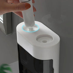 A hand inserts a toothpaste tube into a wall-mounted toothpaste dispenser squeezer with glowing blue rings around the insertion ports.