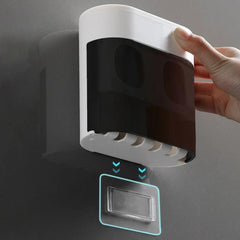 A hand holds a wall-mounted bathroom storage caddy above an adhesive wall mount, with toothbrush holder slots at the caddy's base.
