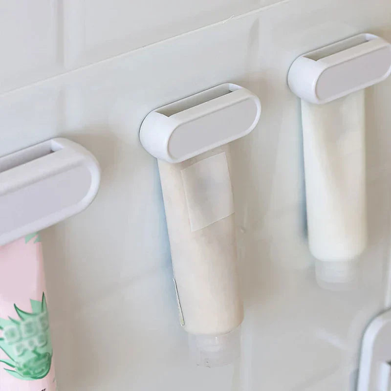 Toothpaste Tube Squeezer - Three white roller clips holding assorted squeeze tubes mounted on a white tiled wall