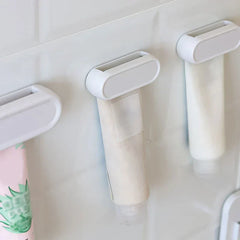 Toothpaste Tube Squeezer - Three white roller clips holding assorted squeeze tubes mounted on a white tiled wall