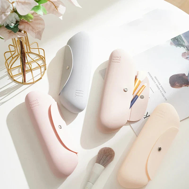 Makeup Brush Holder - Four silicone makeup brush cases in pink, grey, light pink and beige arranged on a white surface, one case open with brushes inside