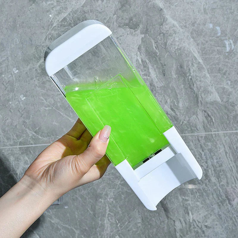 Hand holds a clear travel set bottles dispenser with bright green liquid, white top and base, against a gray tiled wall