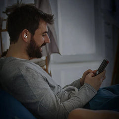 Noise Cancelling Ear Plugs - Person wearing a single ear plug while using a handheld device in bed
