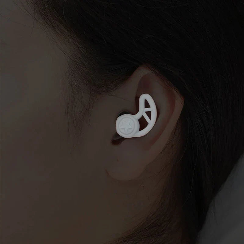 Noise Cancelling Ear Plugs - Close-up of a white silicone earplug worn in a human ear, against dark hair and skin