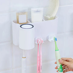 Wall-mounted toothbrush holder mounted on a white tiled wall, holding cups and toothbrushes, with a hand placing an electric toothbrush