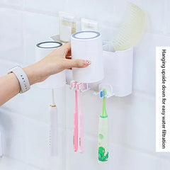 Toothbrush Holder - A hand holds an upside-down white cup above hanging toothbrushes mounted on a wall organizer.