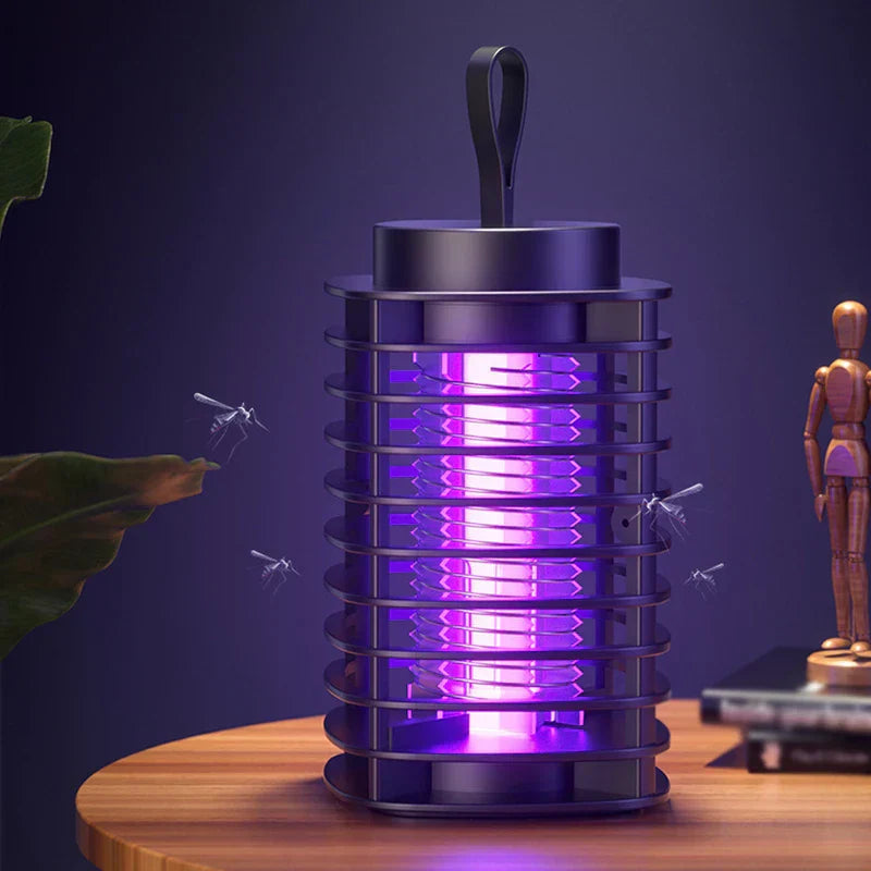 elektrische mückenvernichterlampe - Schwarzes elektrisches Insektenvernichtungsgerät mit leuchtendem violettem UV-Licht auf einem runden Holztisch, Mücken fliegen darauf zu, mit einer hölzernen Gliederpuppe und Pflanzenblättern in der Nähe