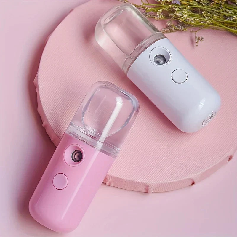 Portable Sprayer - White and pink handheld nano facial misters resting on a pink textured round surface, with dried floral accents in the corner